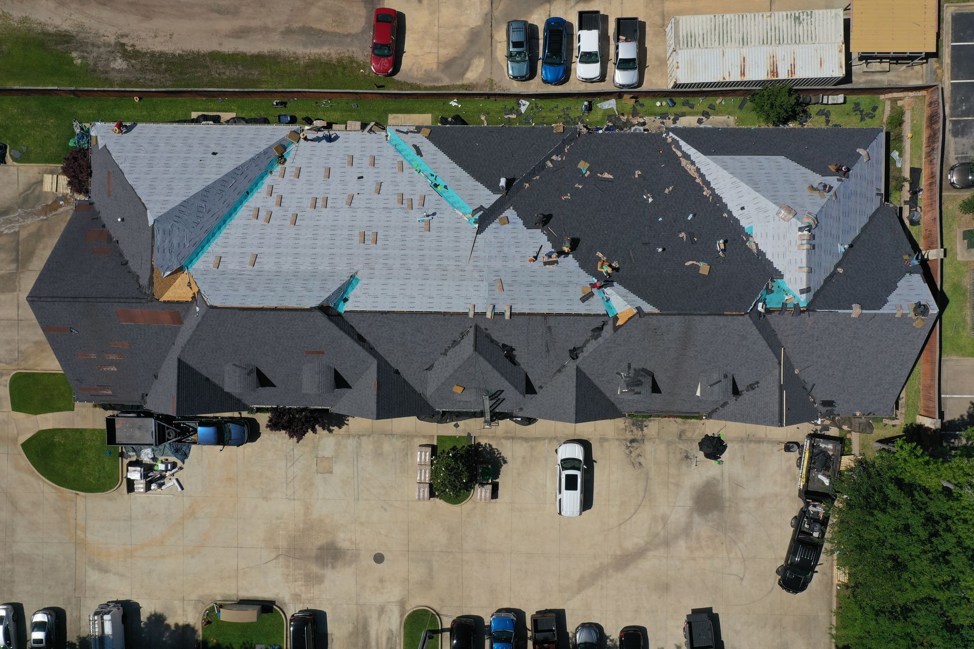 Aerial view of a row of townhouses with partially replaced gray roofing and parked cars nearby