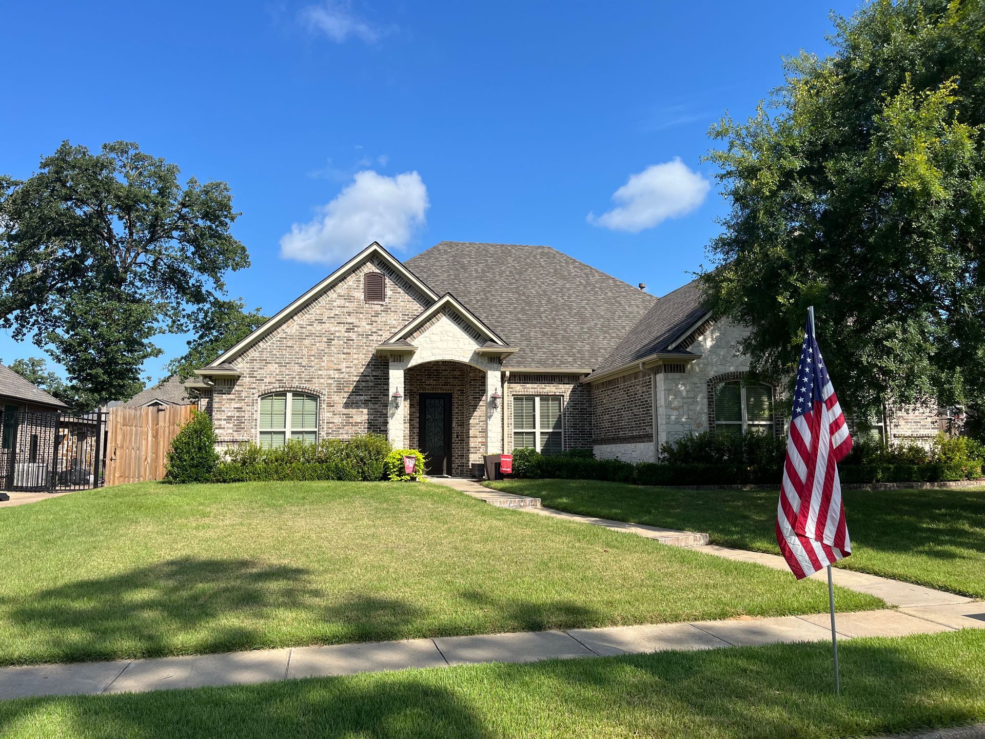 Suburban brick house with a green lawn and an American flag in the front yard