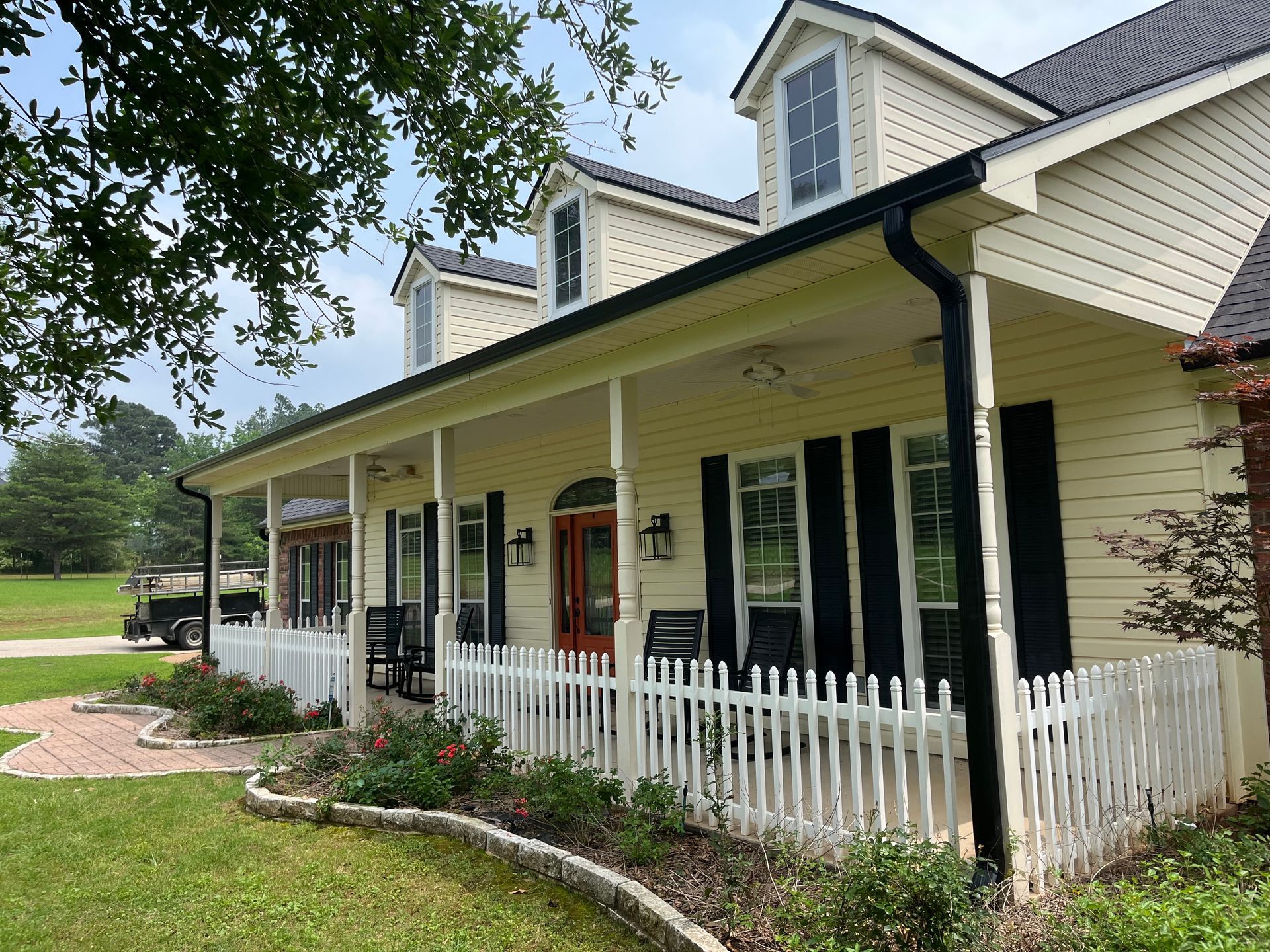 Yellow house with black trim, white picket fence, and porch in a green yard.
