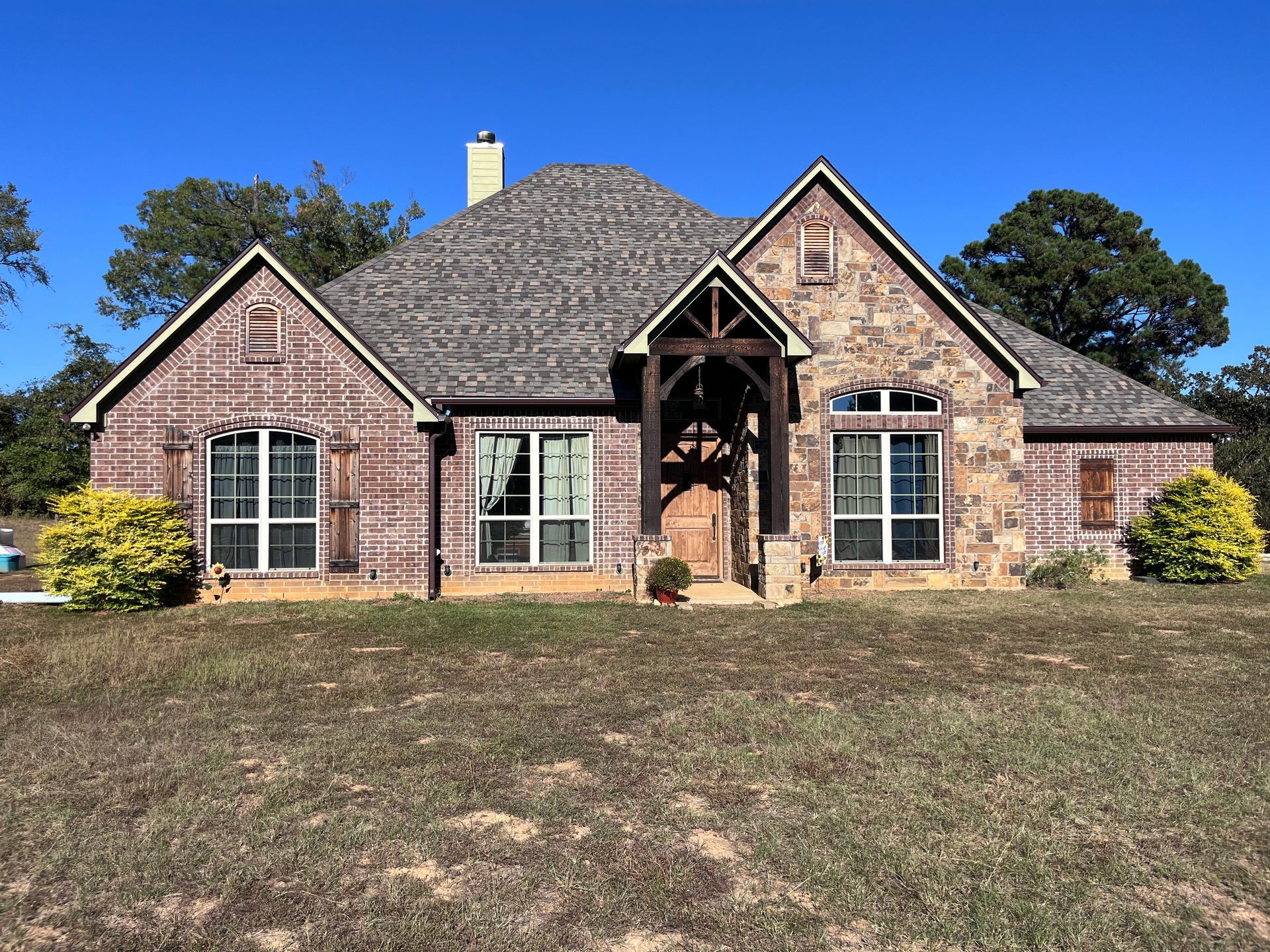 Brick suburban house with a gabled roof, front porch, and large windows on a sunny day