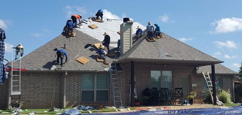 Roofing crew repairing a house roof, with workers on shingles and scaffolding under a blue sky