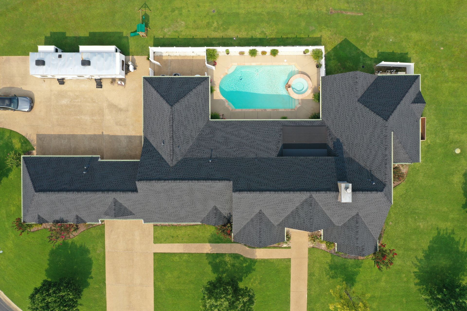 Aerial view of a large house with dark roof, green lawn, and a backyard pool with a patio.