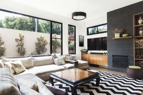 Modern living room with white sectional, black zigzag rug, large windows, and TV wall with shelving