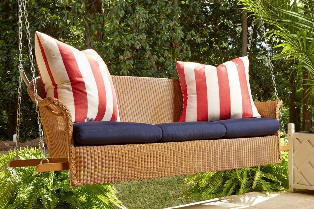 Wicker loveseat with navy seat cushions and red-and-white striped pillows in a garden setting
