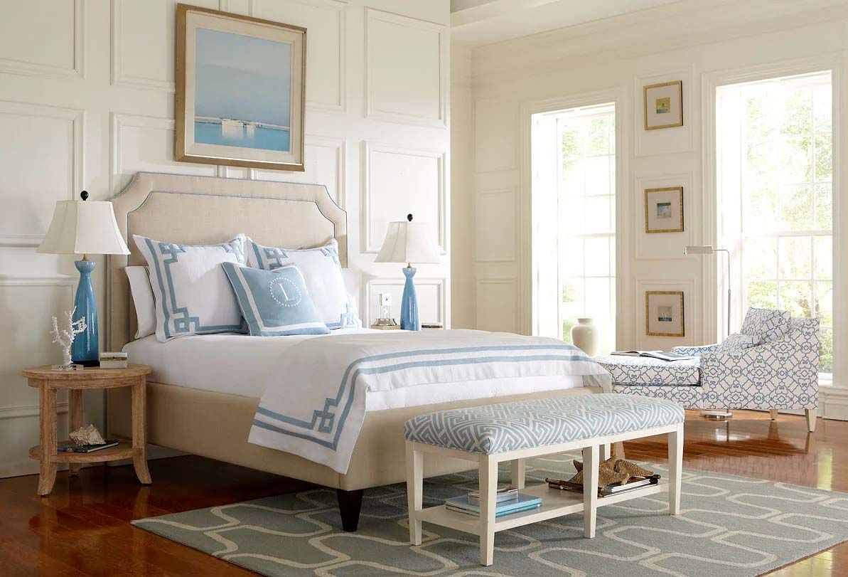 Bright, airy bedroom with a white upholstered bed, blue accents, and a patterned bench at the foot.