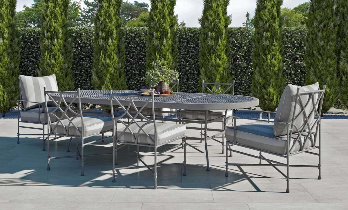 Outdoor patio with metal table and chairs on a sunny terrace, backed by tall evergreen trees.