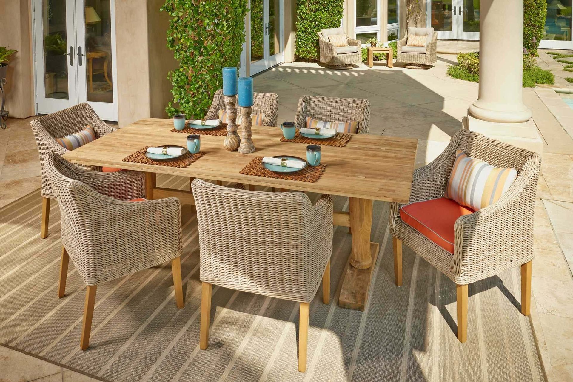 Outdoor dining table with wicker chairs, blue dishes, and striped pillows on a sunny patio