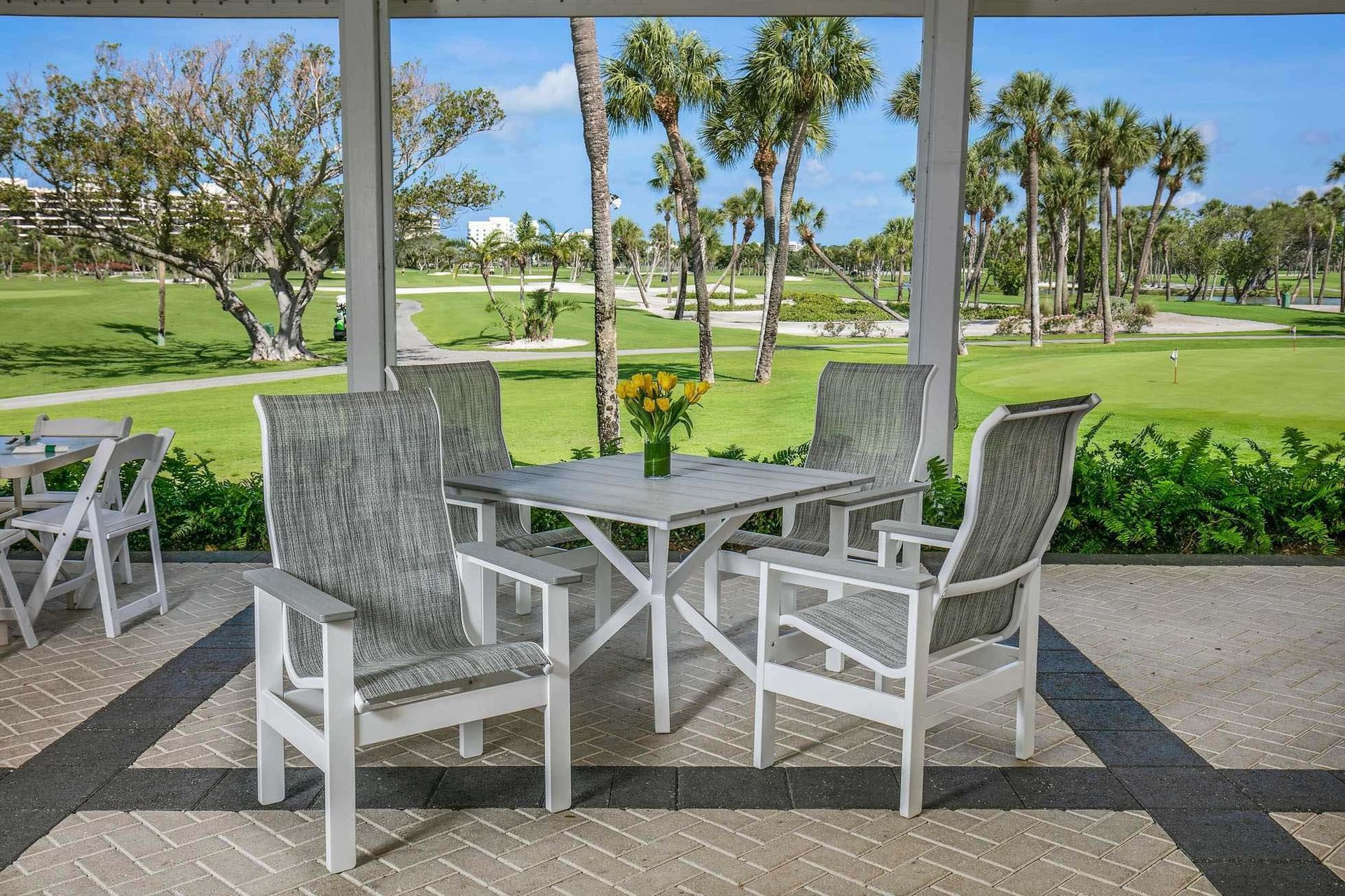 White patio chairs and table on a covered terrace overlooking a green golf course.