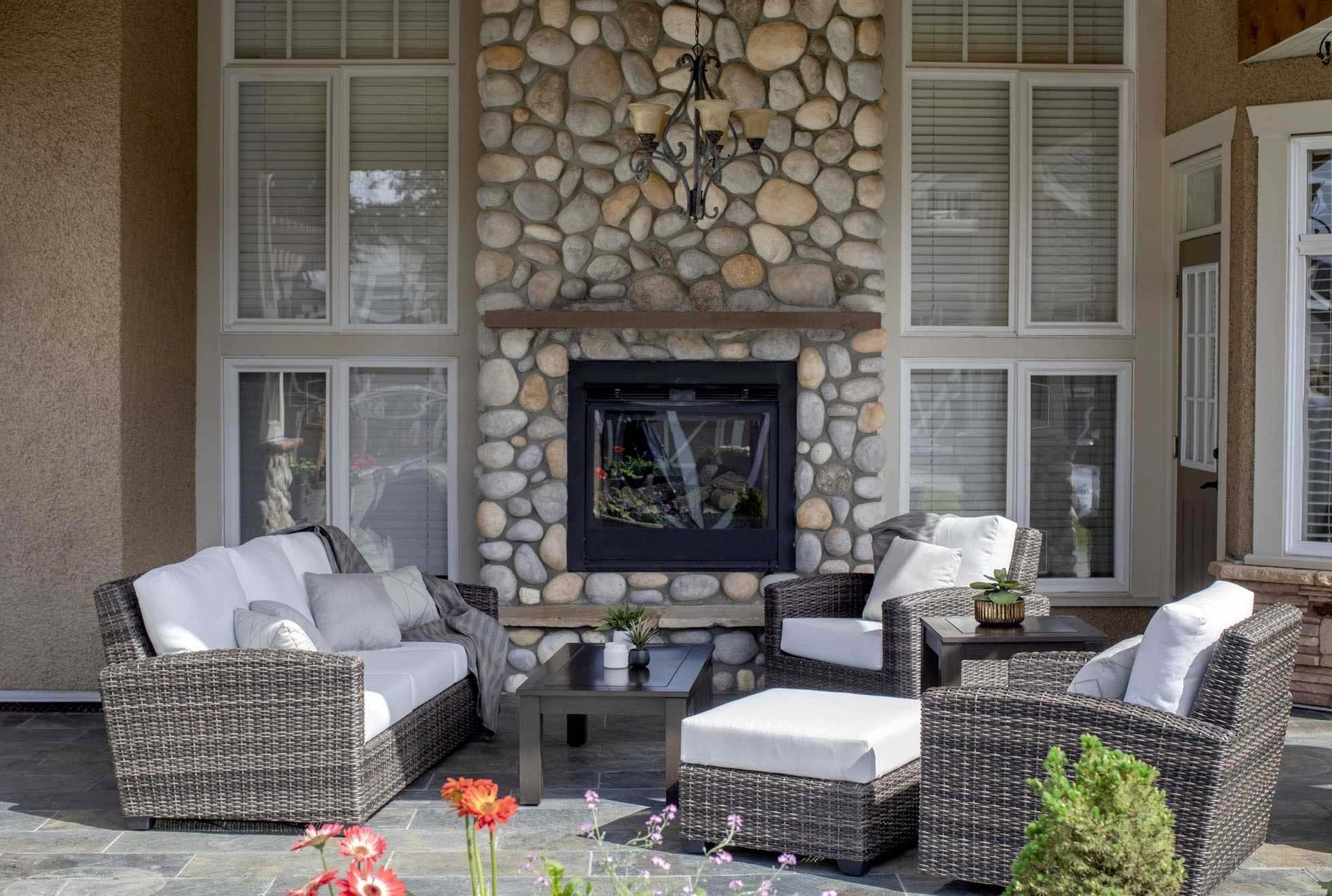 Stone fireplace with wicker patio seating and white cushions on a covered porch