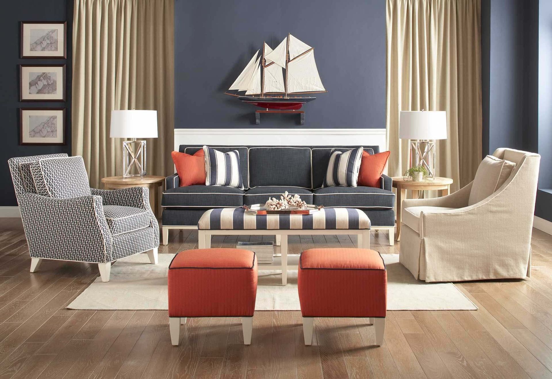 Bright living room with navy sofa, two armchairs, red ottomans, lamps, and sailboat wall art
