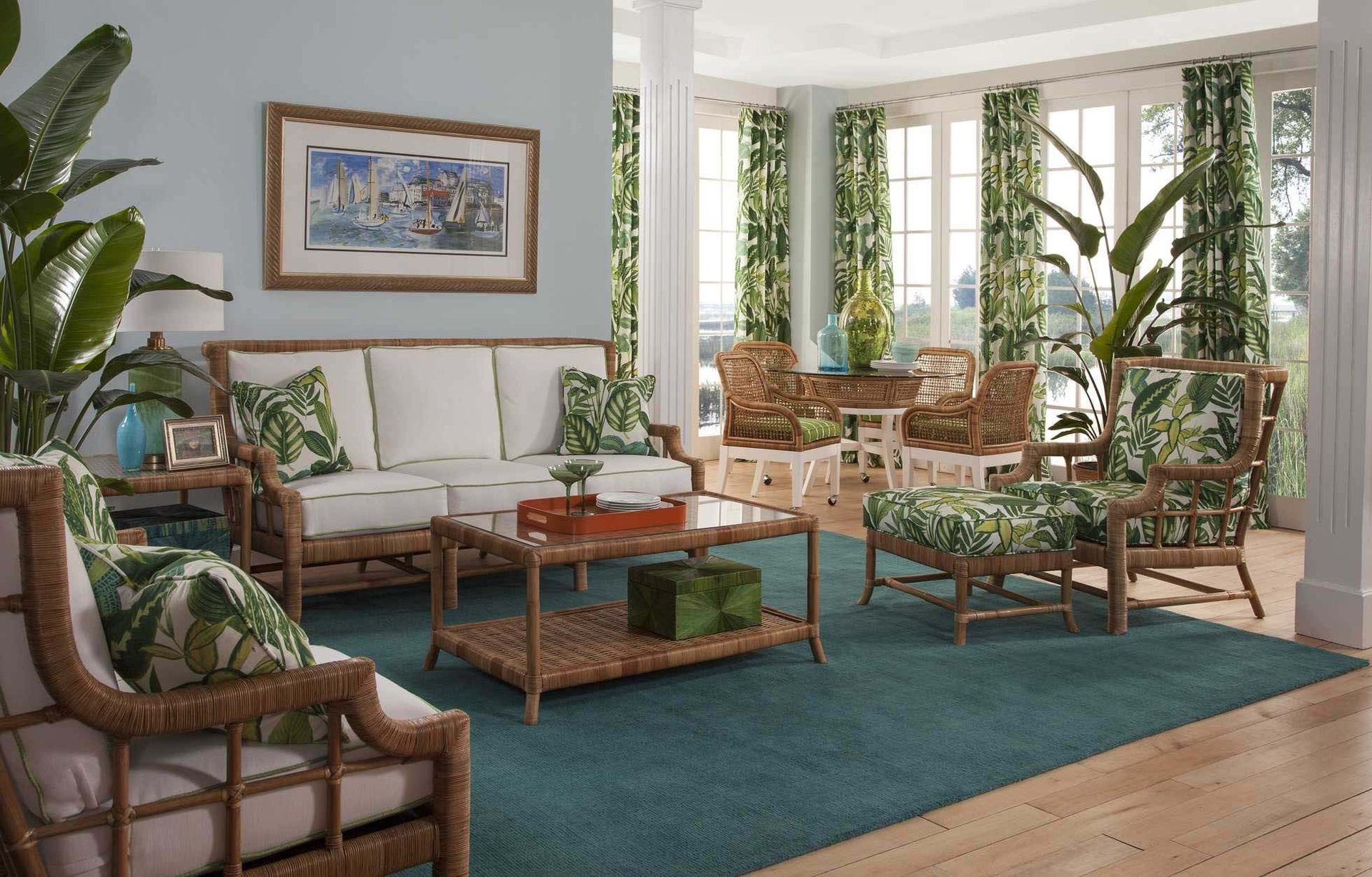 Bright living room with white sofas, wicker chairs, teal rug, and large windows overlooking greenery