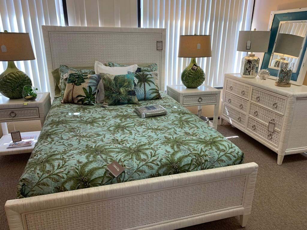 White wicker bed with green floral bedding in a bright bedroom, flanked by lamps and matching bedside tables