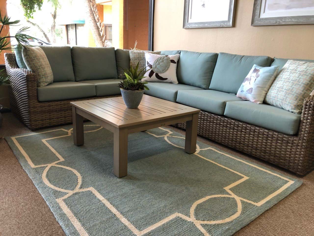 Cozy patio seating with wicker sectional sofa, coffee table, and teal rug in a bright living area