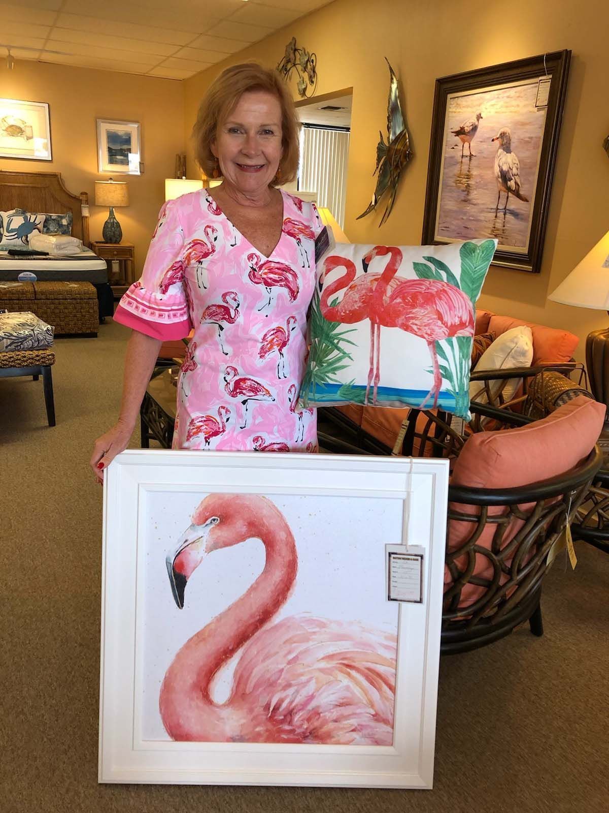 Woman in pink holding flamingo paintings in a cozy living room.
