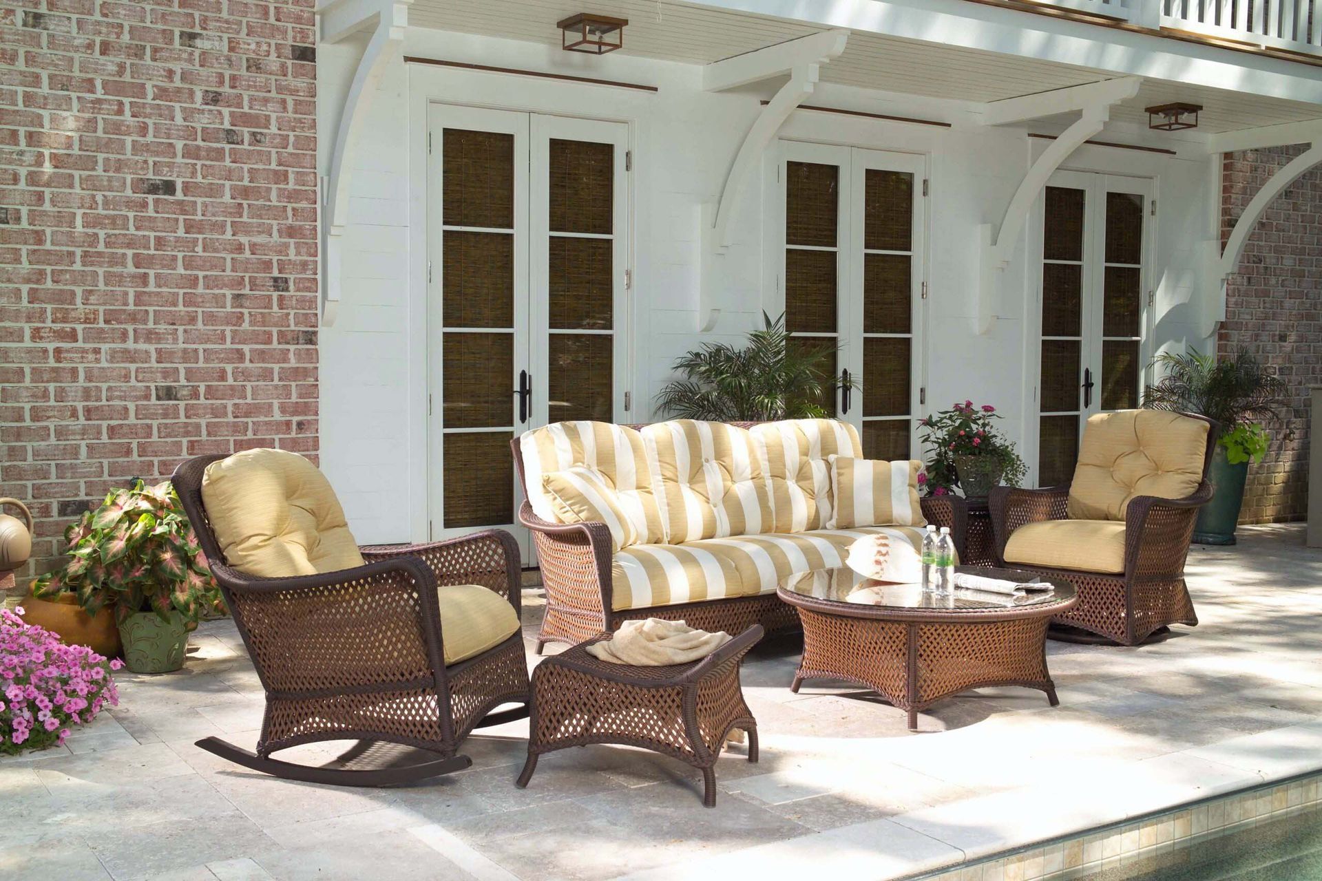 Patio seating set with wicker chairs, striped cushions, and a coffee table outside a brick house