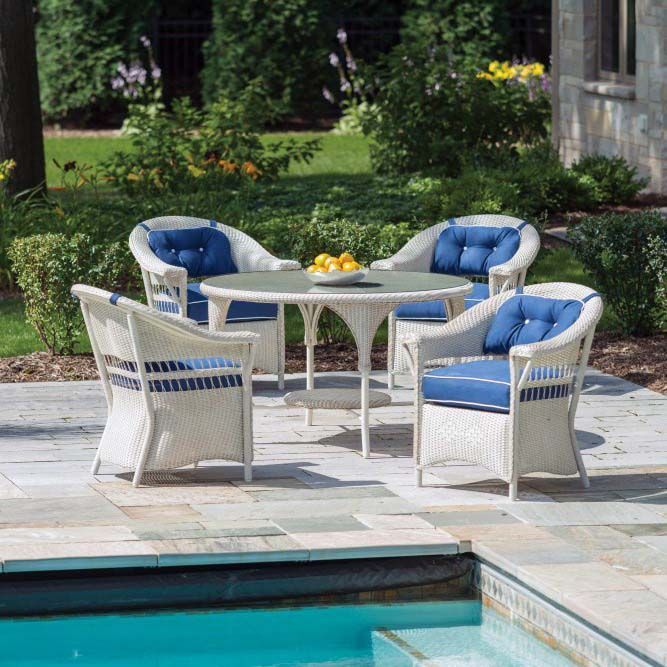 White wicker patio chairs with blue cushions around a small table beside a pool.