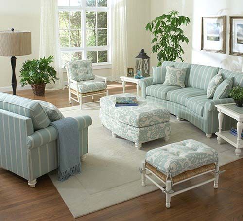 Bright living room with pale blue striped furniture, cream rug, plants, and large windows.