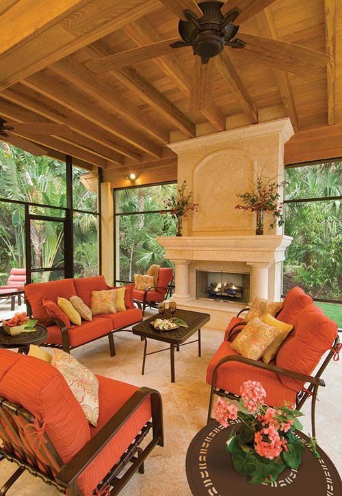 Cozy sunroom with orange sofas, a fireplace, and large windows under a wooden ceiling