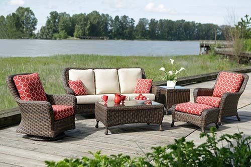 Outdoor patio seating set with red patterned chairs, cream sofa, and glass coffee table by a lake