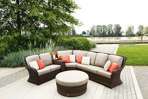 Outdoor patio seating with curved beige and brown sectional sofa, round ottoman, and green lawn backdrop