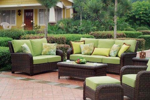 Outdoor patio seating with green cushions and dark wicker furniture on a brick terrace