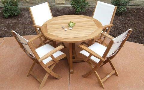 Round wooden patio table with four folded white-cushioned chairs on a patio