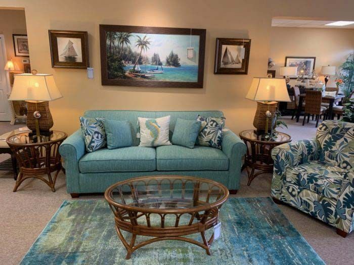 Living room with teal sofa, patterned chairs, glass coffee table, and ocean painting above fireplace