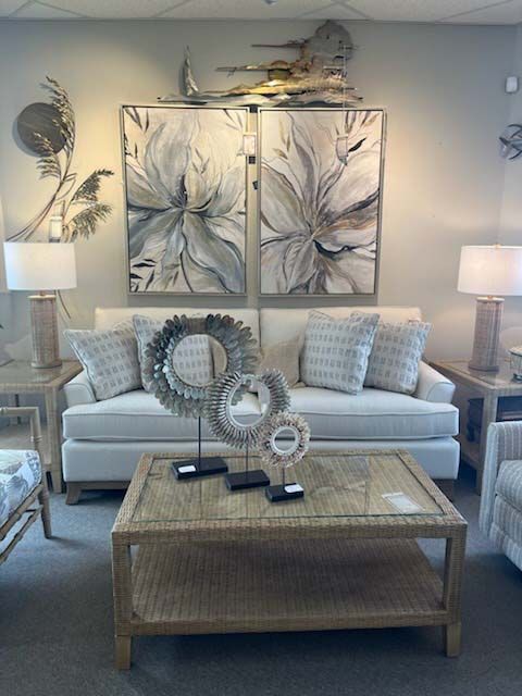 Neutral-toned living room with white sofa, wicker coffee table, lamps, and abstract wall art.