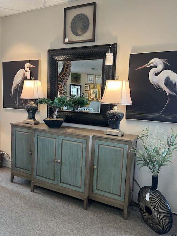 Teal sideboard with lamps and mirror, flanked by black swan art in a neutral room.