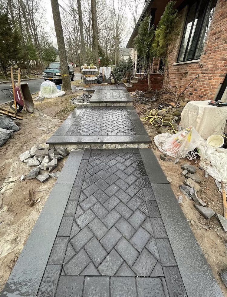 Brick walkway under construction with a dark gray herringbone pattern.
