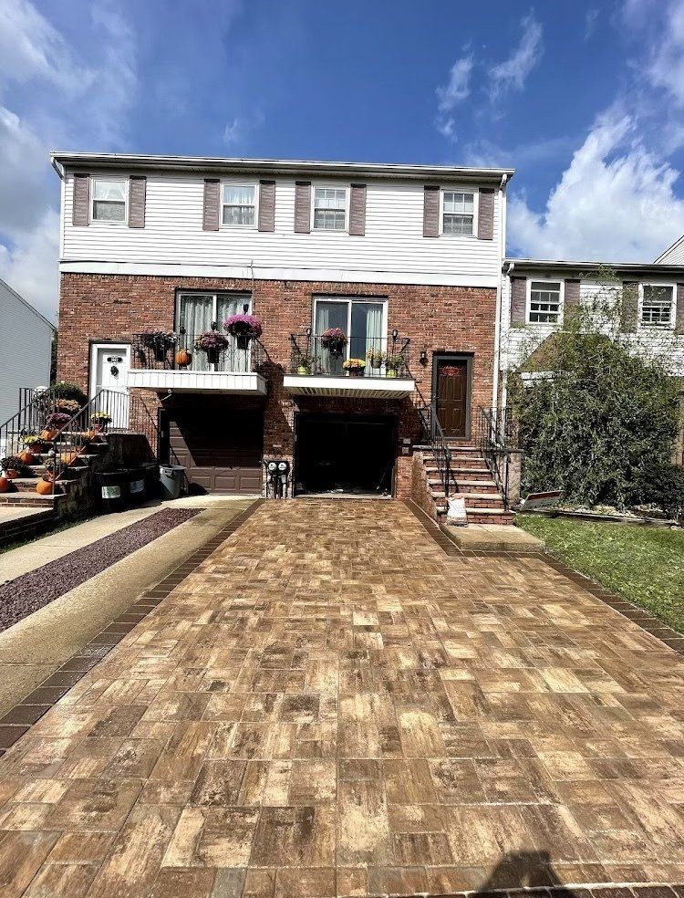Two-story house with brick facade, brown driveway, and flower pots. Blue sky.