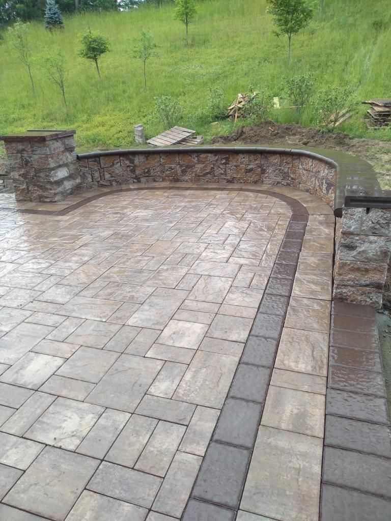Stone patio with a low stone wall and pillars, built-in seating, and a grassy hill in the background.
