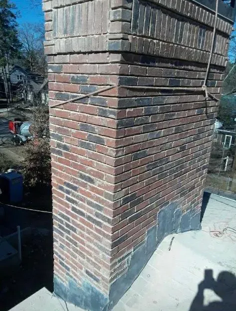 Brick chimney on a rooftop, with alternating red and black bricks. A light blue sky is visible.