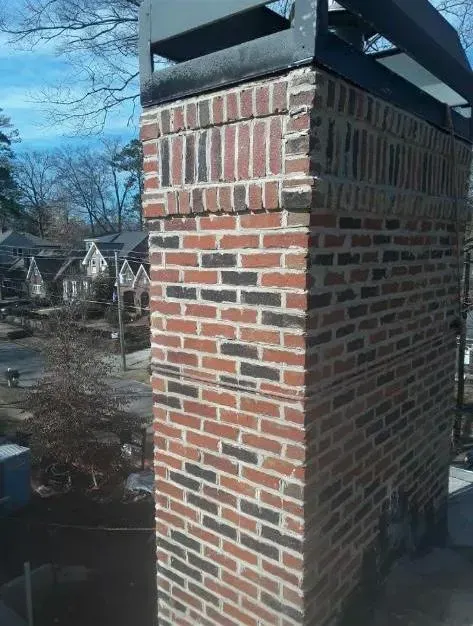 Brick chimney with metal cap against a blue sky, houses in the background.