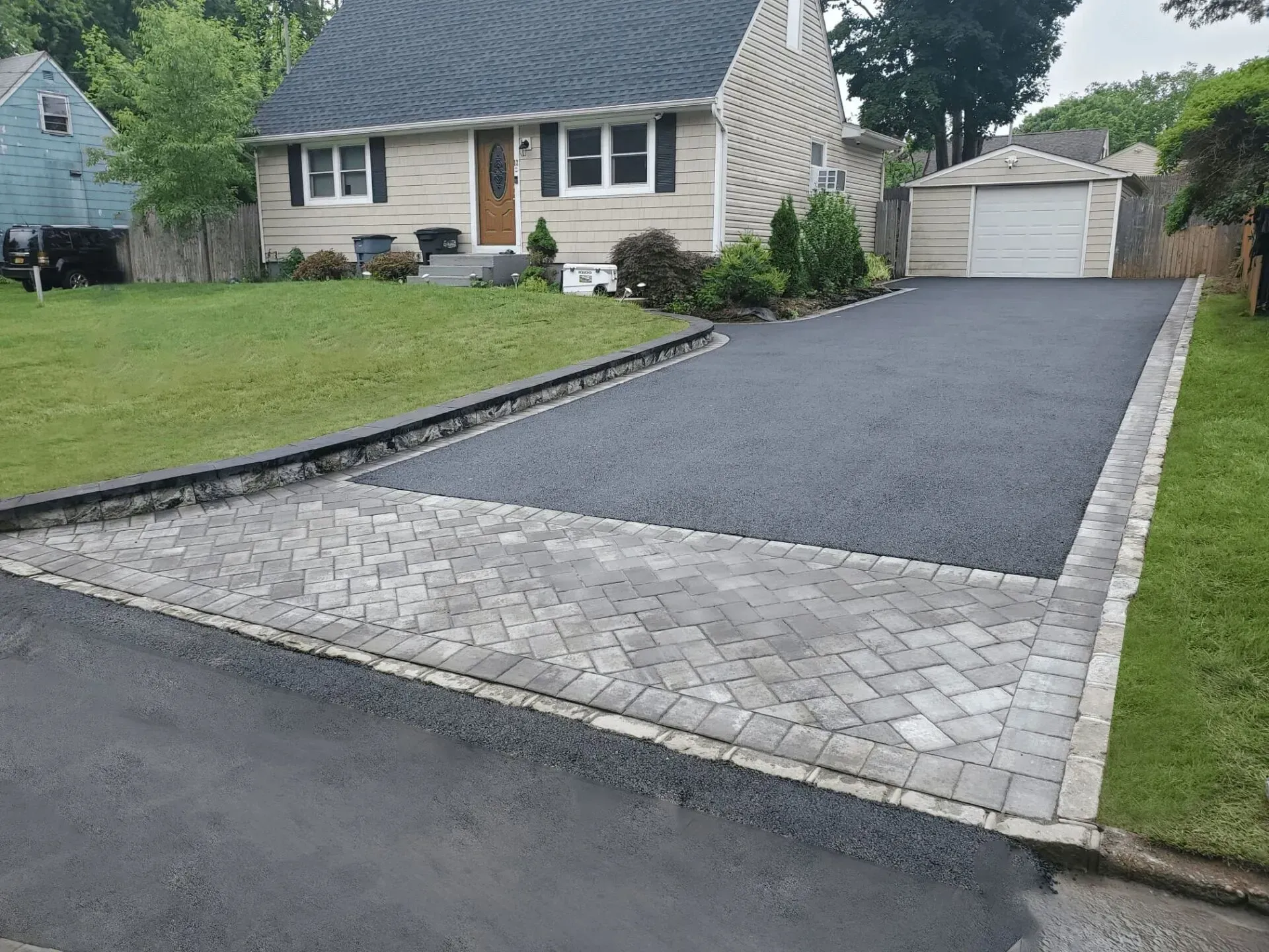 A house with a paved driveway transitioning from brick to asphalt.