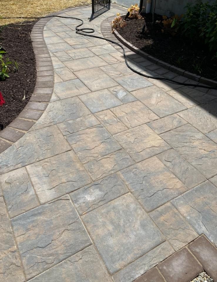 Stone walkway with brown edging, winding through a garden bed, dark hose running across.