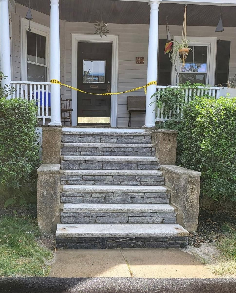 Stone steps leading to a porch with columns and a closed front door, yellow tape across the entrance.