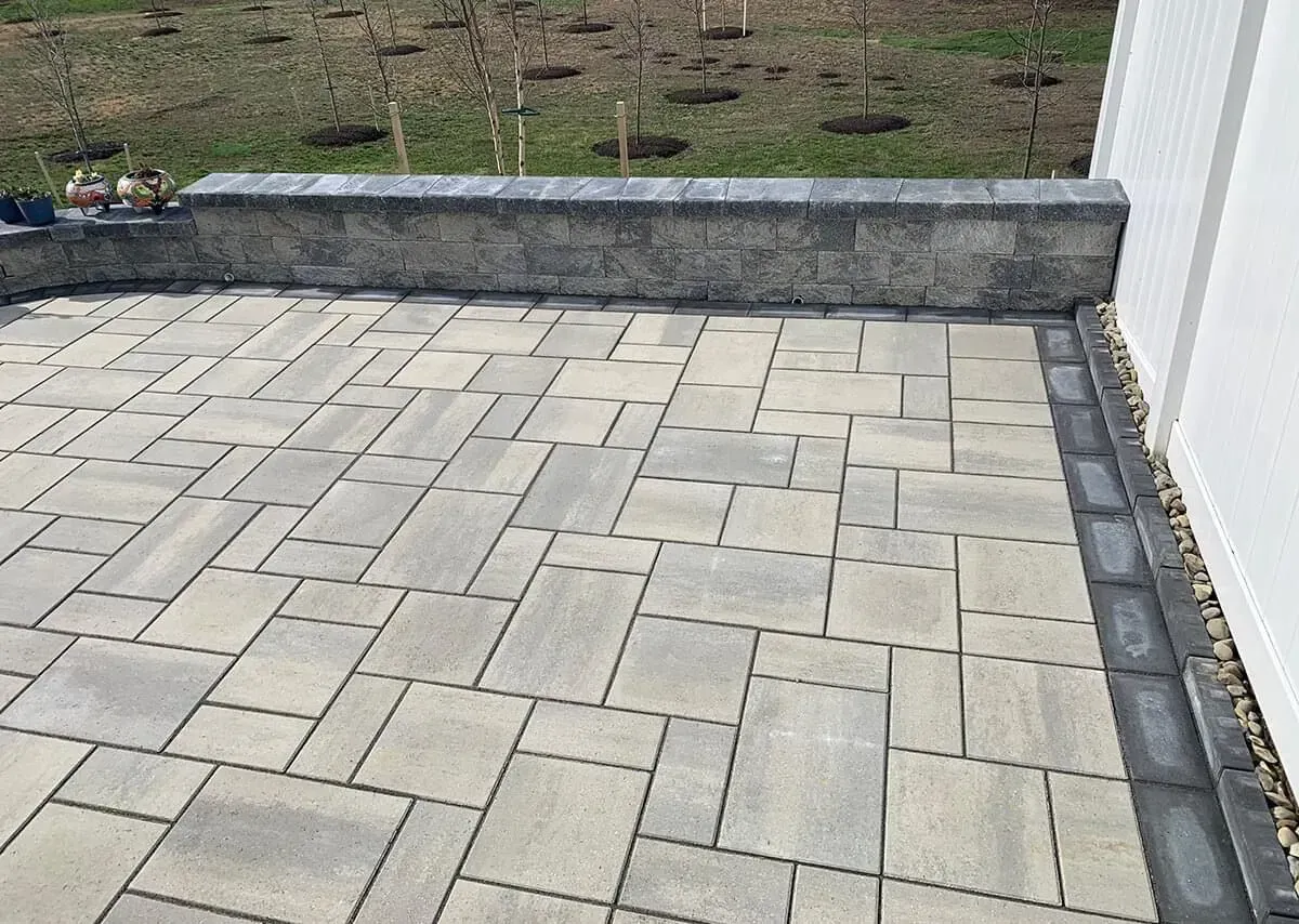 Stone patio with a low retaining wall and a white fence.