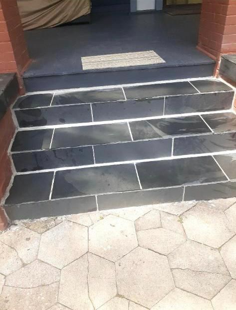 Steps leading to a door, black tiles, white grout, red brick sides, and a light brown rug.