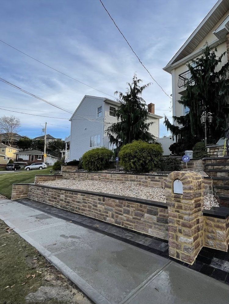 A brick retaining wall with a gravel bed in front of a house. Sidewalk in foreground.