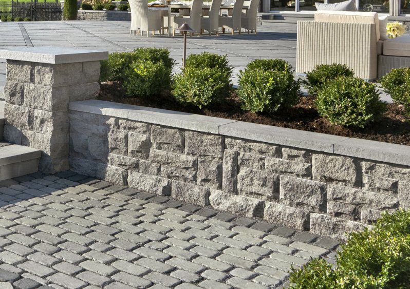 Stone retaining wall with pavers, planted with green shrubs.