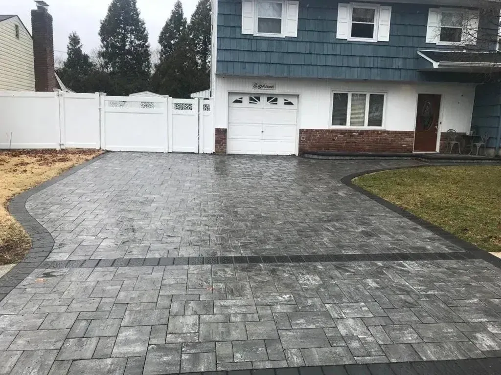 Brick driveway leading to a two-story house with white fence and garage.