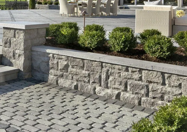 Stone retaining wall with boxwood shrubs, paving stones, and a patio setting.