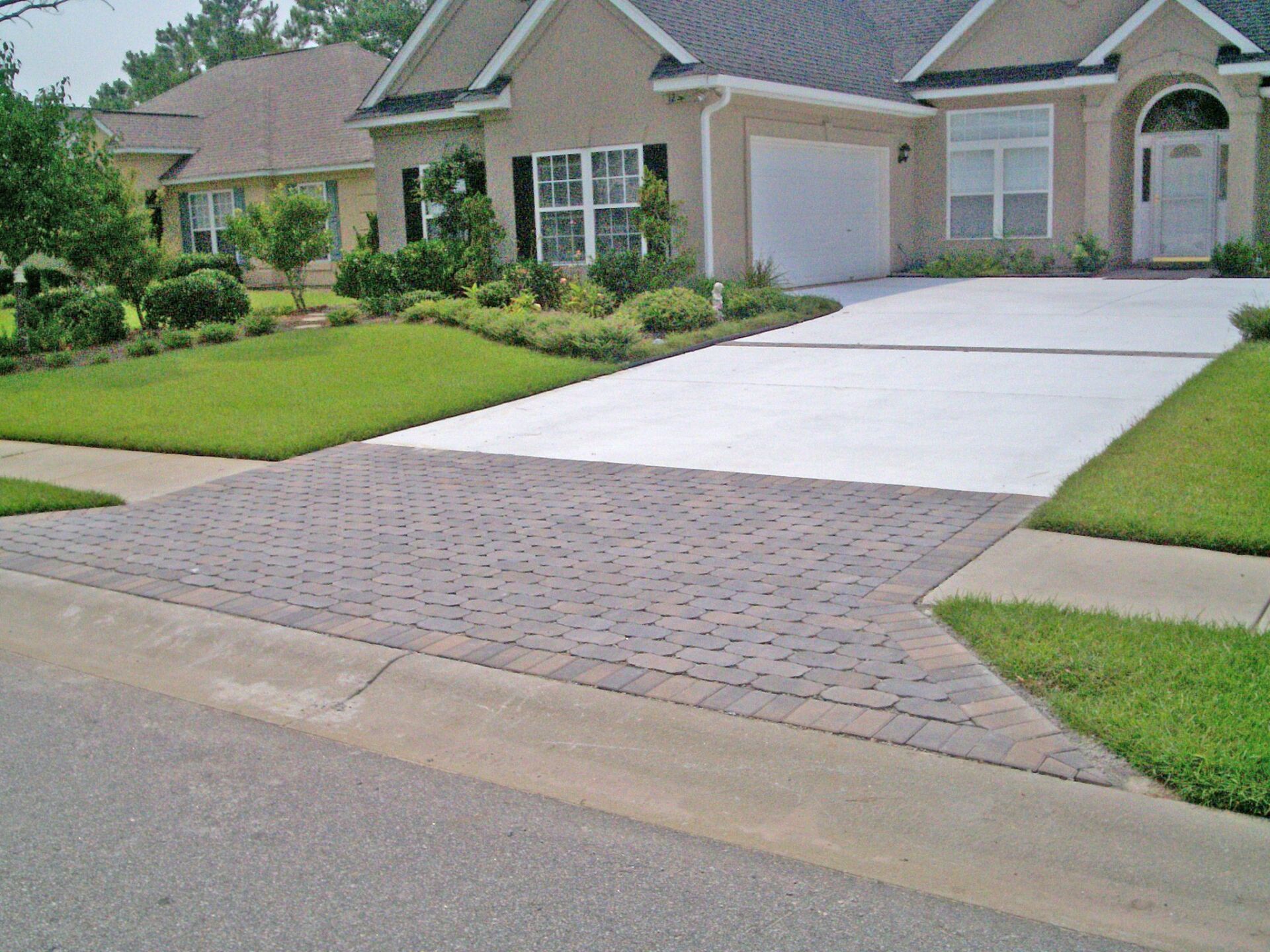 Brick driveway transitioning to concrete, leading to a house with a garage.
