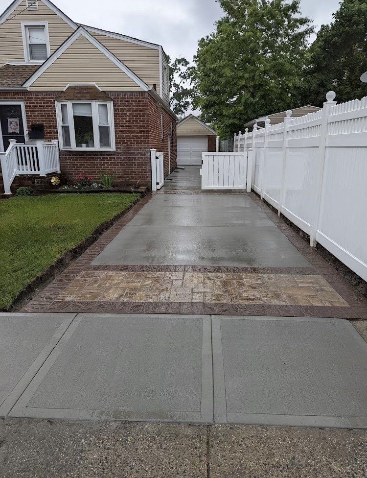 Driveway leading to a house with a brick facade, flanked by grass and a white fence.