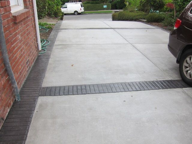 Concrete driveway with dark brick edging and a car parked on the right.