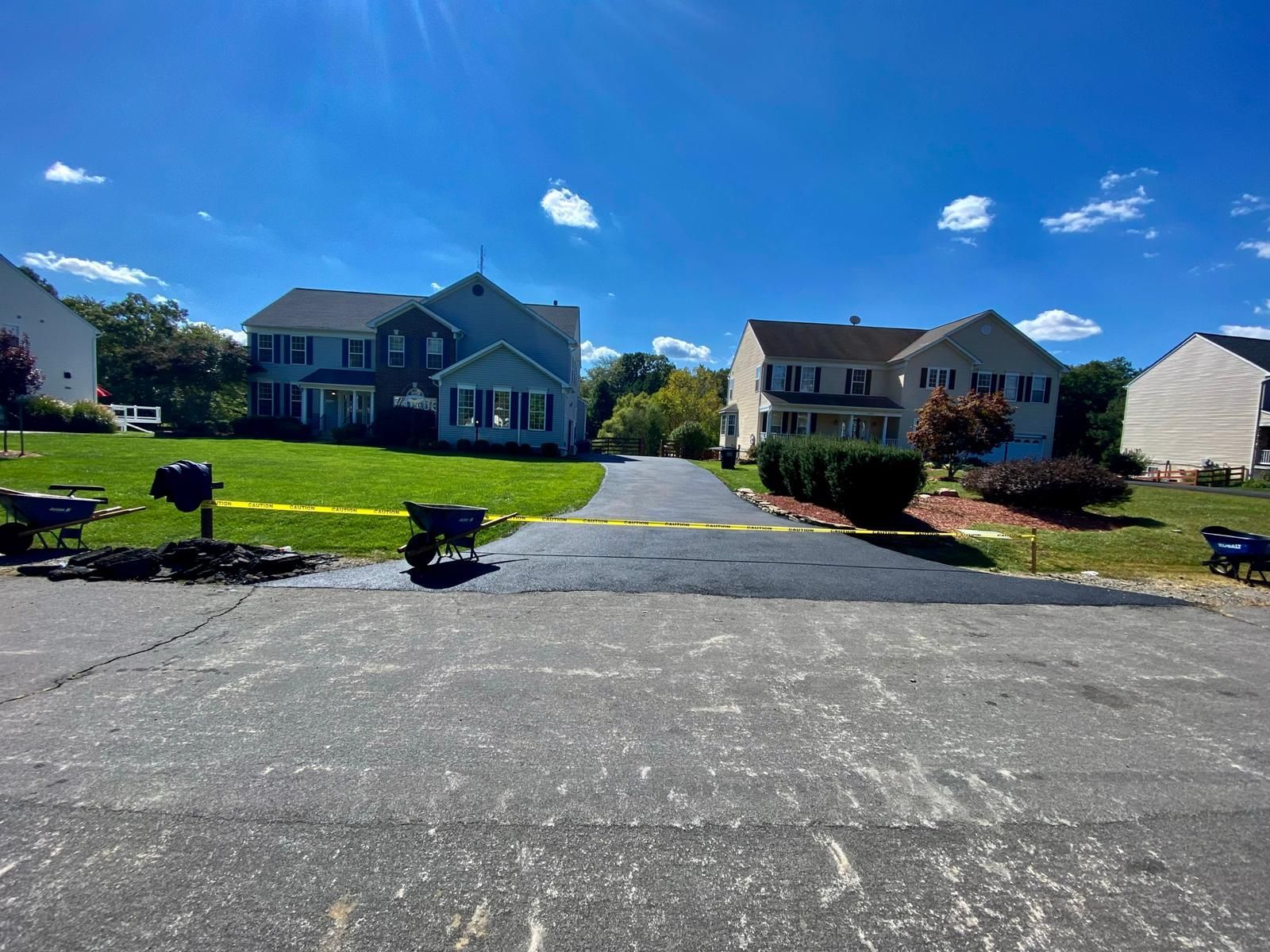 Asphalt driveway being paved in front of two-story houses on a sunny day.