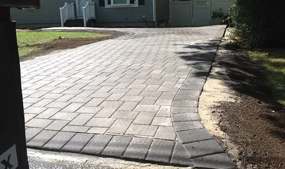 Brick paver driveway in front of a house with green grass on either side.