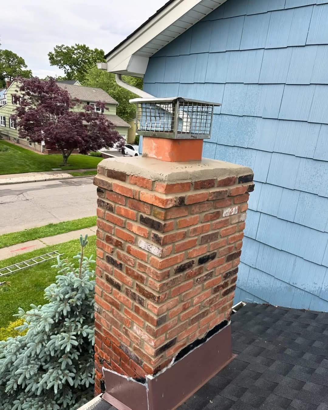 Brick chimney with a metal cap atop a house with blue siding.
