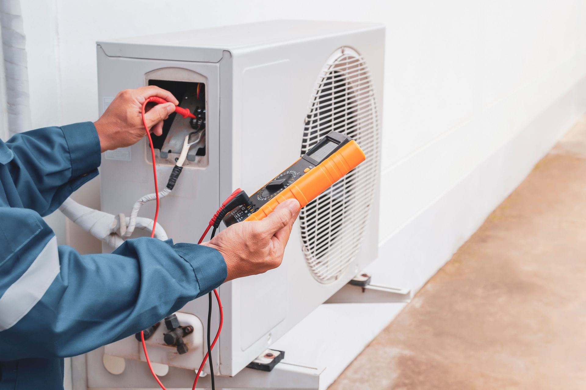 Technician testing HVAC unit wiring with a multimeter and orange clamp meter outdoors